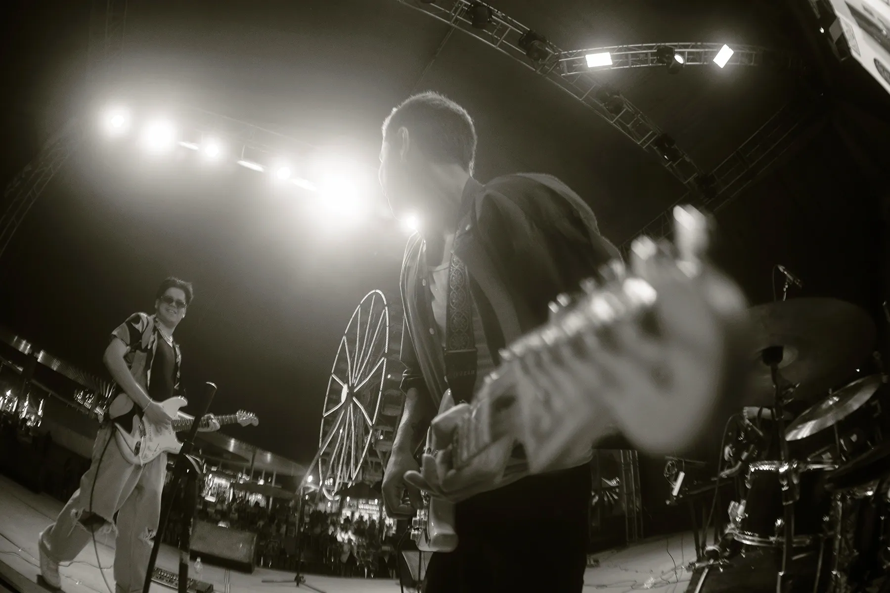 Guitarristas en escenario nocturno con rueda de la fortuna al fondo, foto en blanco y negro