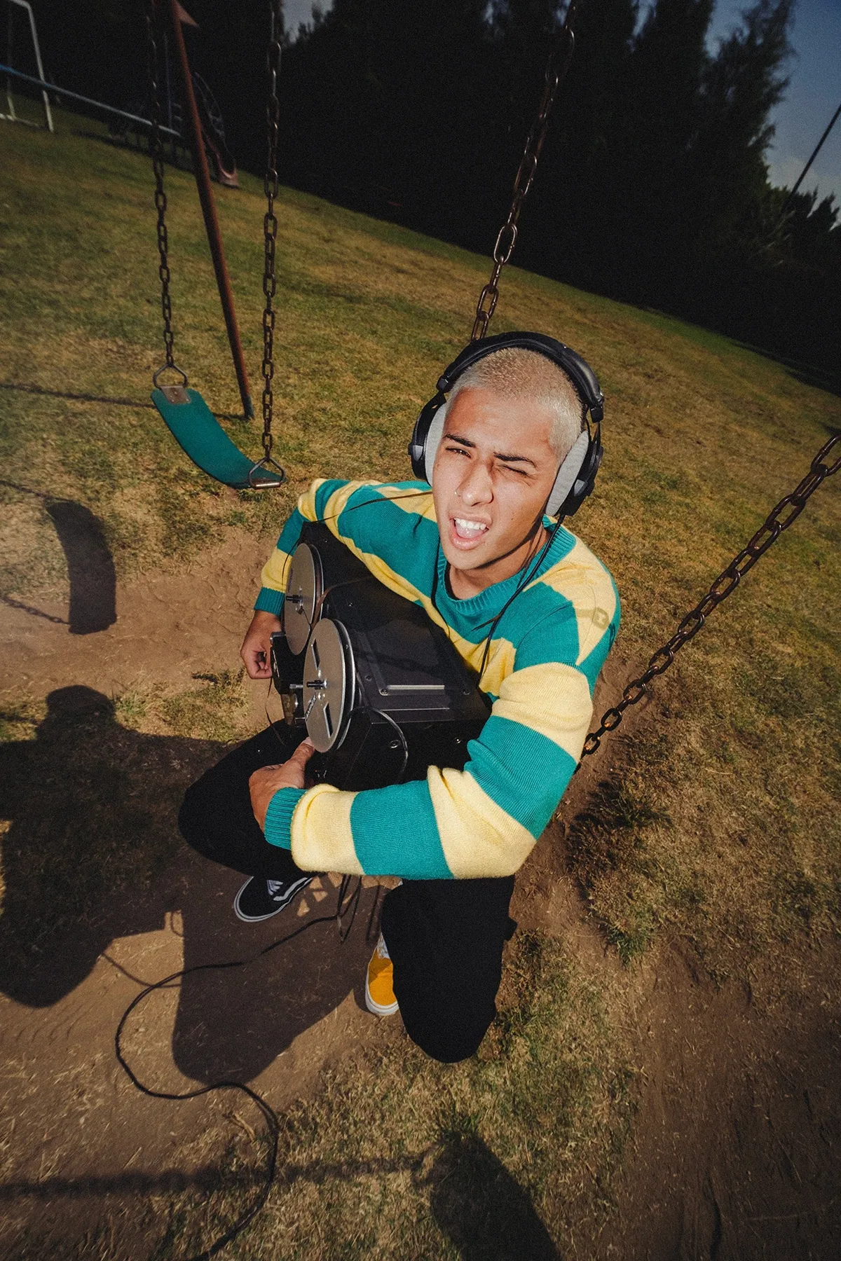 Galo Barker arrodillado en un columpio con una grabadora de carrete